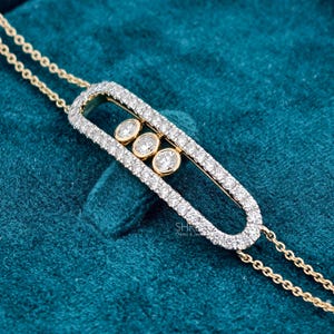 May include: A gold bracelet featuring an elongated oval frame encrusted with small round diamonds. Inside the frame, three round diamonds are set in gold bezels. The bracelet is attached to a delicate gold chain on both sides of the oval frame.