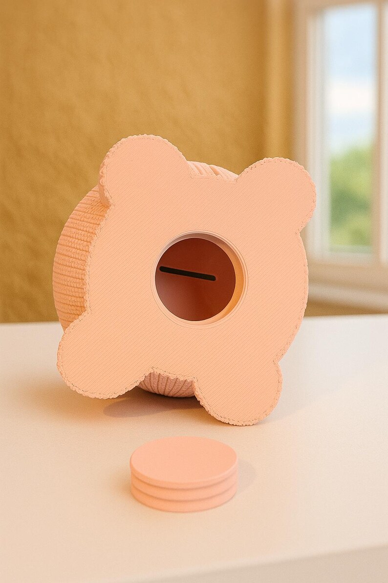 May include: A peach-colored piggy bank with a round coin slot and a stack of matching coasters. The bank has a textured, knitted body and a four-lobed top. The design is simple and modern, suitable for a nursery or a child's room.