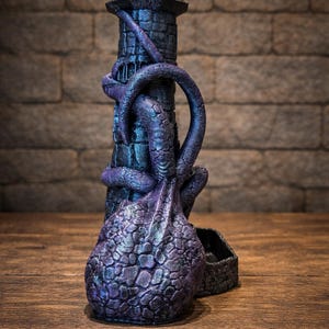 May include: A dark purple and black dice tower shaped like a stone lighthouse wrapped in tentacles. The structure features a textured, scaly surface and a base with a tray for dice. The top of the tower has a pointed roof, and the logo FATES END 2026 YEAR OF THE HORSE is visible in the upper left corner.
