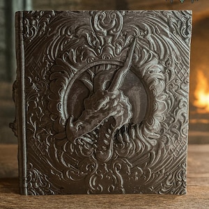 Könnte beinhalten: Ein dunkelbraunes, aufwendig geschnitztes Buch mit einem Drachenkopf als Mittelpunkt. Der Einband zeigt kunstvolle Verzierungen und einen kreisförmigen Rahmen um den Drachen. In der oberen rechten Ecke steht "2025" und "FATESEND YEAR OF THE SNAKE".