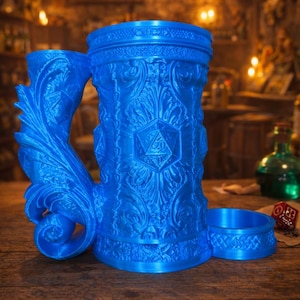 Op de afbeelding: Een blauwe, 3D-geprinte mok met ingewikkelde bloemen- en geometrische ontwerpen, waaronder een D20-dobbelsteen. De mok heeft een bijpassende onderzetter en een gedetailleerde handgreep. De mok is gemarkeerd met "Fates End" en "2026".