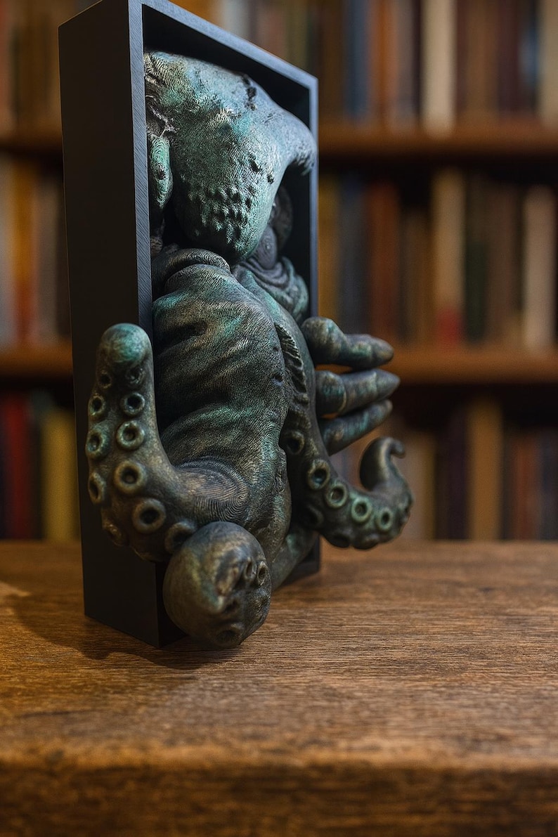 May include: A detailed sculpture of a creature with tentacles, emerging from a black rectangular frame. The sculpture has a weathered, greenish-bronze finish. The background is a blurred bookshelf.