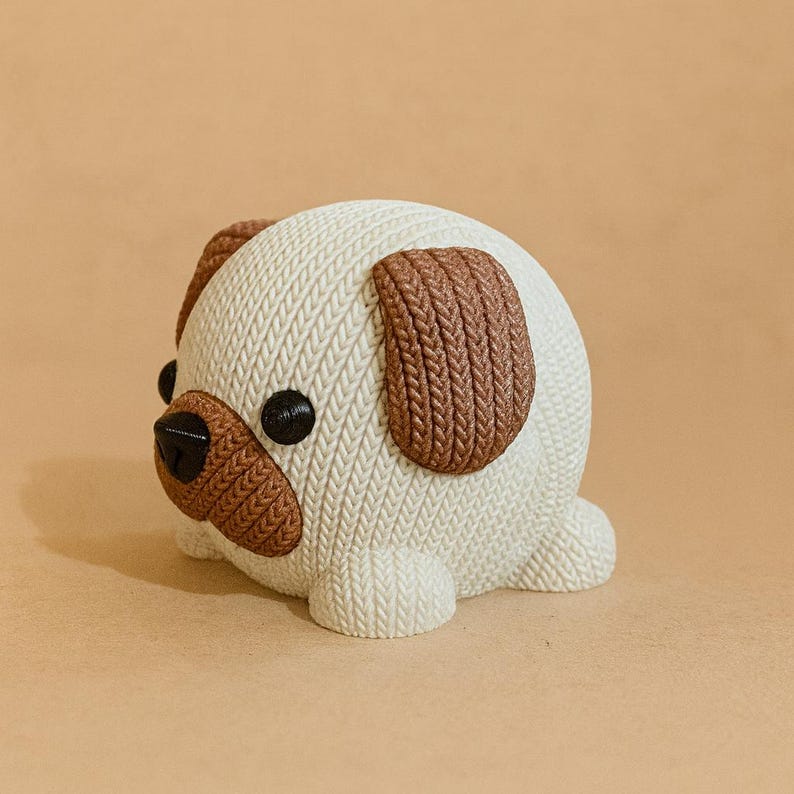 May include: A ceramic pug figurine with a textured, knitted appearance. The pug has a white body, brown ears, and a brown snout. It has black eyes and is lying down. The figurine is on a solid tan background.