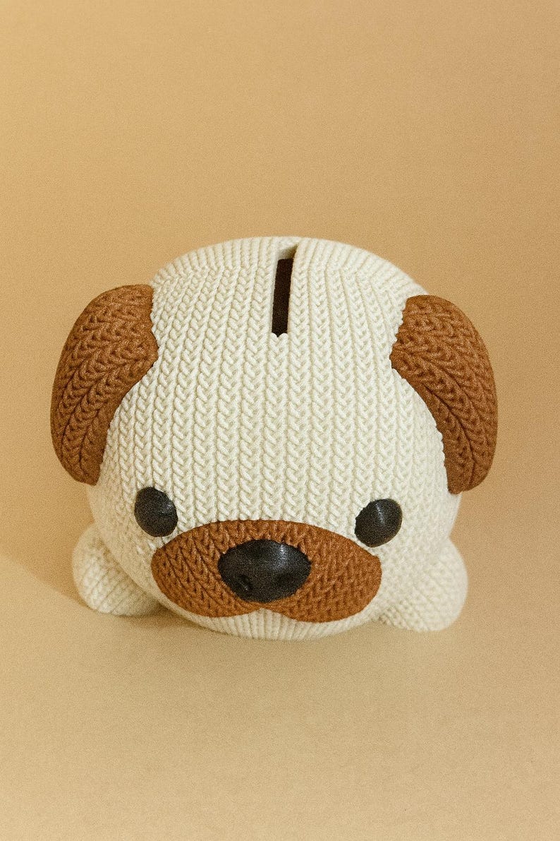 May include: A ceramic pug-shaped piggy bank. The bank is white with brown accents on the ears, snout, and around the eyes. It has a slot on top for inserting coins and is a decorative item.