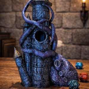 May include: A dark stone tower dice tower featuring a large purple tentacle wrapped around the structure, with a circular opening in the center and a textured base. Several multi-sided gaming dice are positioned near the base of the tower.