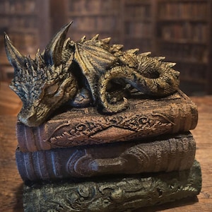 Könnte beinhalten: Eine detaillierte Skulptur eines Drachen, der auf drei gestapelten, kunstvoll geschnitzten Büchern ruht. Der Drache ist gold- und bronzefarben, mit komplizierten Schuppen und Flügeln. Die Bücher sind in verschiedenen Braun- und Grüntönen gehalten, mit detaillierten Reliefmustern. Der Text "Fates End" und "Year of the Horse" ist enthalten.