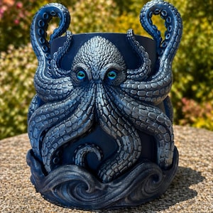 Könnte beinhalten: Ein dunkelblauer Blumentopf mit Oktopus-Motiv, detaillierten Tentakeln und strukturierter Oberfläche. Der Oktopus hat auffällige blaue Augen und ist an der Basis von stilisierten Wellen umgeben. Dieser dekorative Pflanztopf ist für den Innen- und Außenbereich geeignet.