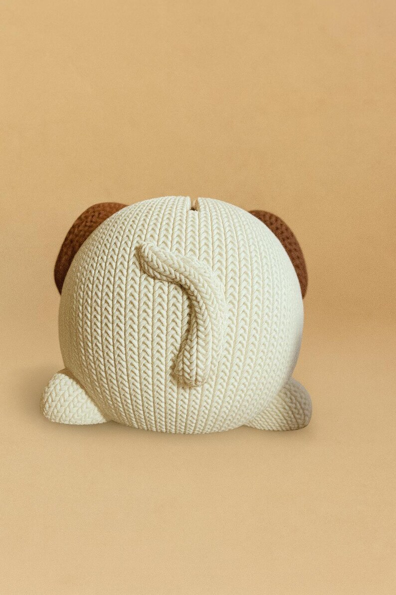 May include: A ceramic dog-shaped bank with a textured, off-white body and brown ears. The dog's tail curls upwards. The bank has a slot on top for inserting coins. The design resembles a knitted sweater.
