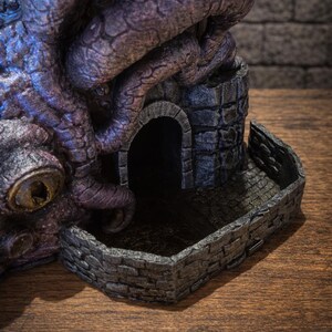 May include: A purple and blue textured dice tower featuring a large eye and winding tentacles wrapped around a stone structure with an arched doorway and a low brick wall enclosure. A logo in the corner reads FATES END 2026 YEAR OF THE HORSE.