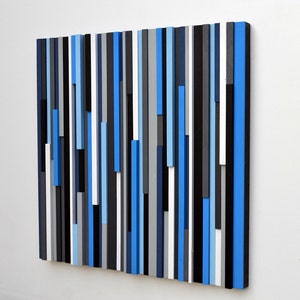 May include: Abstract wall art made of vertical wooden strips in shades of blue, black, white, and gray.