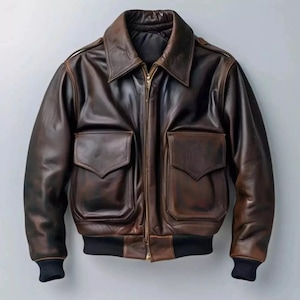 Könnte beinhalten: Braune Leder-Bomberjacke mit Reißverschluss, zwei Vordertaschen und schwarzem Rippsaum und Bündchen. Die Jacke hat einen klassischen Kragen und einen Vintage-Look.