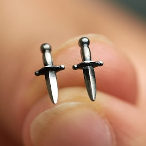 May include: A pair of silver dagger earrings. The earrings are small and delicate, and they have a sharp point.