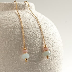 May include: A pair of gold chain threader earrings featuring a small round pink bead and a larger faceted pale blue bead at the end of each chain. The earrings are constructed with delicate gold-tone metal chains and small gold-coloured spacer beads.