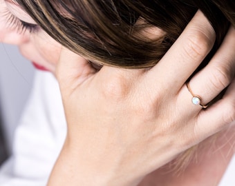 May include: A gold ring with a white opal gemstone. The ring is on a person's finger.