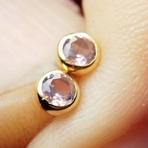 May include: A pair of gold stud earrings with small, round, light pink gemstones.