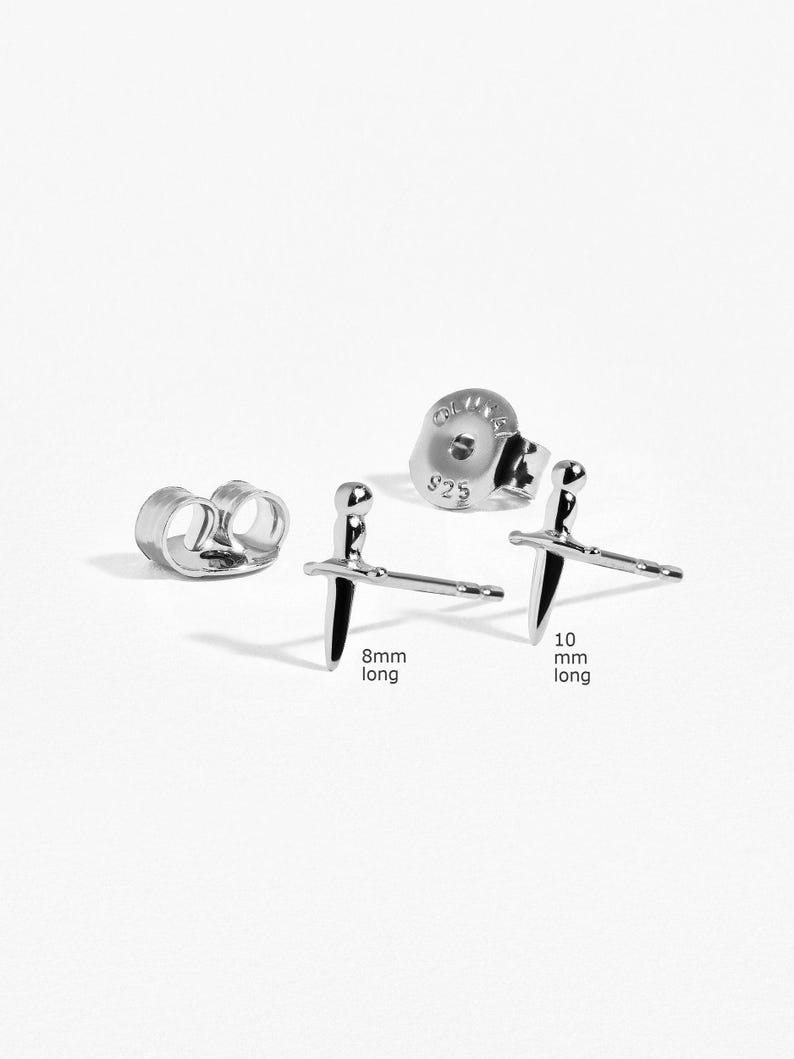 May include: Two silver-toned sword-shaped stud earrings with matching earring backs. One earring post is labeled 8mm long and the other is labeled 10mm long. The earring backs are stamped with 925, indicating sterling silver composition.