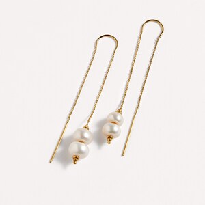 May include: A pair of gold dangle earrings with two white pearls on each earring.