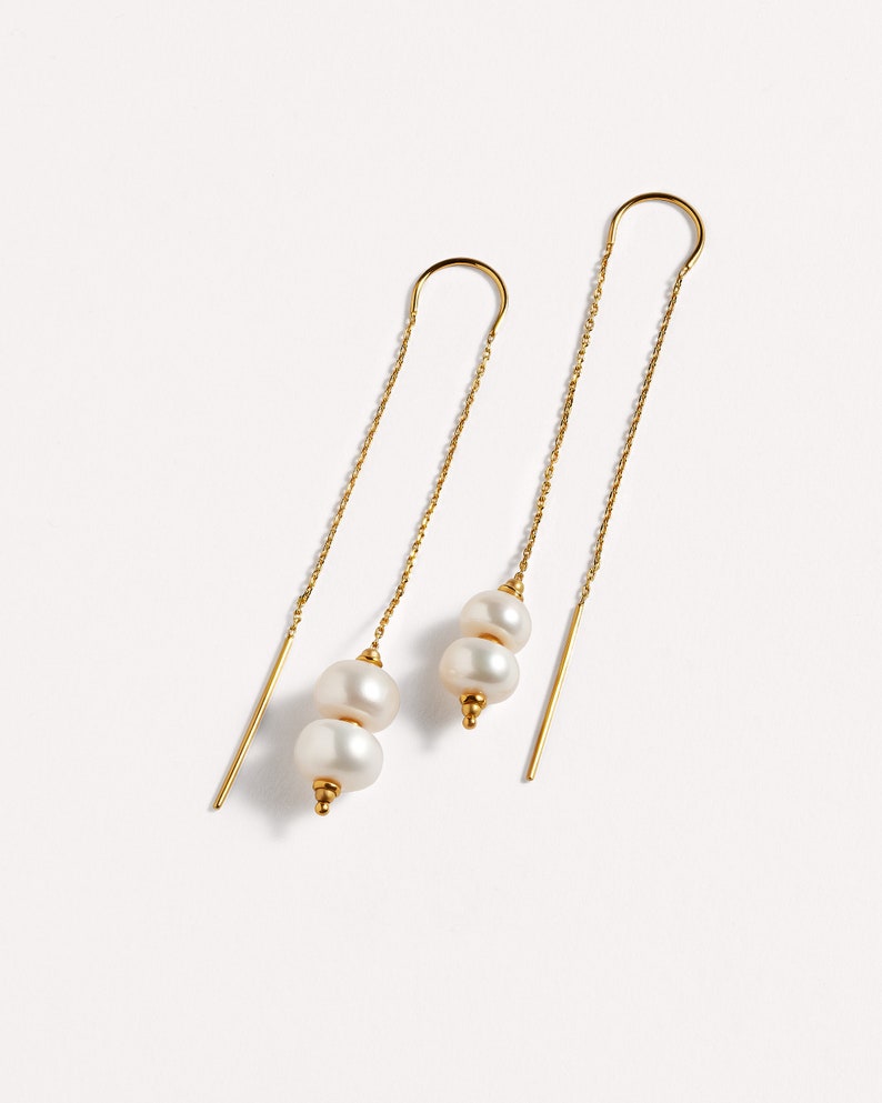 May include: A pair of gold dangle earrings with two white pearls on each earring.