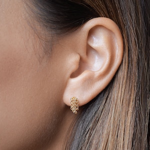 May include: A gold stud earring featuring a cluster of delicate, fine-linked chains that hang vertically from the earlobe. The earring has a polished metallic finish and a compact design, creating a subtle, layered appearance on the ear.