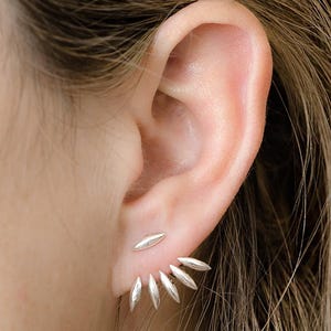 May include: A silver ear climber earring featuring a series of six polished, marquise-shaped metal segments that follow the curve of the earlobe. The design consists of a single top piece and a larger, fan-like arrangement of five connected pieces.