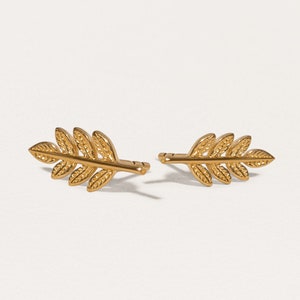 May include: A pair of gold leaf stud earrings. The earrings are made of a delicate, textured metal and feature a simple, elegant design.