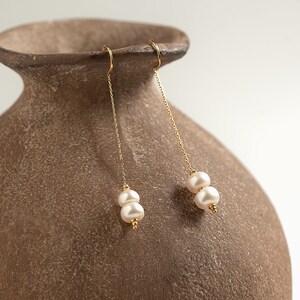 May include: A pair of gold dangle earrings with two white pearls on each earring.