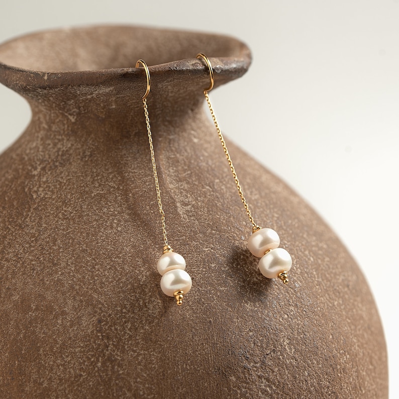May include: A pair of gold dangle earrings with two white pearls on each earring.