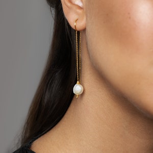 May include: Gold chain earrings with a single white pearl dangling from the end of each chain.