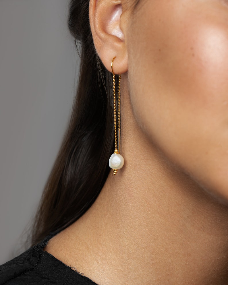May include: Gold chain earrings with a single white pearl dangling from the end of each chain.