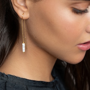 May include: A pair of gold dangle earrings with a white bead chain. The earrings are long and delicate, and the beads are small and round.