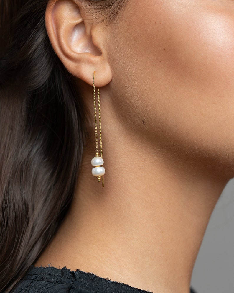 May include: Gold chain earrings with two white pearl accents.