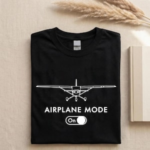 A black t-shirt with a white graphic of an airplane and the text "AIRPLANE MODE" printed on it, along with a button that says "On".