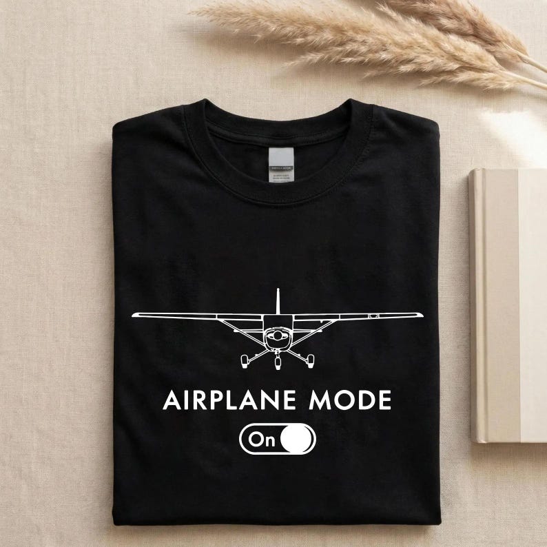 A black t-shirt with a white graphic of an airplane and the text "AIRPLANE MODE" printed on it, along with a button that says "On".