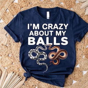 May include: Navy blue t-shirt with the text "I'M CRAZY ABOUT MY BALLS" in white. The shirt features two snake illustrations, one black and white, the other brown and orange. The shirt is knotted at the bottom.