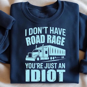 May include: Navy blue sweatshirt with the text "I DON'T HAVE ROAD RAGE YOU'RE JUST AN IDIOT" in light blue. A light blue graphic of a semi-truck is centered below the text. The sweatshirt has a crew neck and long sleeves.