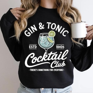 May include: Black sweatshirt with a white graphic that reads "GIN & TONIC Cocktail Club" with a cocktail glass illustration. The design includes the text "ESTD 1840s" and "THERE'S SOMETHING FOR EVERYONE!"