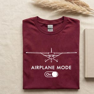 A maroon t-shirt with a white graphic of an airplane and the text "AIRPLANE MODE" printed on it, along with a power icon.