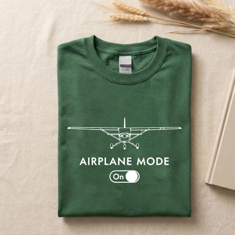 A green t-shirt with a white graphic of an airplane and the text "AIRPLANE MODE" printed on it, along with a button that says "On".