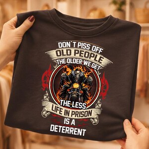 a person holding a black t-shirt with a graphic design and text on it.