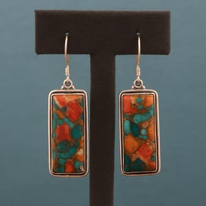 Może przedstawiać: Srebrne prostokątne kolczyki wiszące z mozaiką czerwonych, turkusowych i pomarańczowych kamieni. Kamienie osadzone są w srebrnej ramie i zawieszone na srebrnym haczyku.