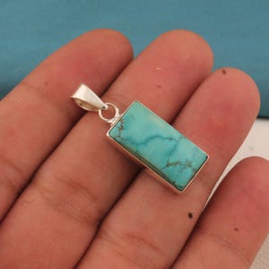 May include: A rectangular turquoise pendant with a silver-colored metal frame and bail. The turquoise stone has a light blue-green color with brown veining. The pendant is designed to be worn as a necklace.
