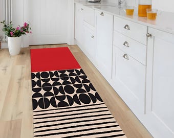 May include: A rectangular kitchen runner rug with a striking geometric pattern. It features a red top section, a black and cream half-circle design, and black stripes on a cream base. The rug is laid on a light wooden floor, suitable for a kitchen.