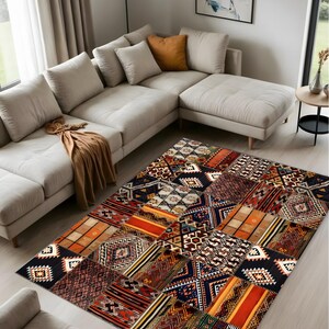 May include: A colorful patchwork rug with geometric and tribal patterns in shades of red, orange, black, and brown. The rug is placed on a light-colored wooden floor, with a beige sectional sofa in the background.