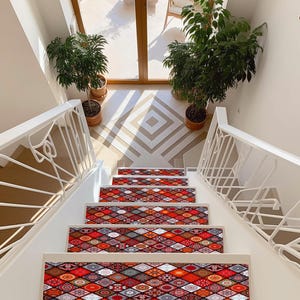 May include: A staircase with white steps and patterned stair treads in red, orange, and brown. The treads have a geometric design. White railings and potted plants are on either side of the stairs. The flooring at the top of the stairs has a geometric pattern.
