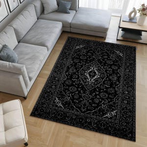 May include: A black area rug with an ornate, traditional design. The rug features a central medallion and floral patterns in a lighter color, creating a contrast against the dark background. The rug is placed on a wooden floor, near a light-colored sectional sofa.