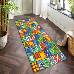 Op de afbeelding: Een rechthoekig, kleurrijk vloerkleed met een patchwork-ontwerp. Het vloerkleed heeft een verscheidenheid aan geometrische en abstracte vormen in levendige kleuren zoals rood, blauw, geel en groen. Het vloerkleed ligt op een donkere houten vloer.