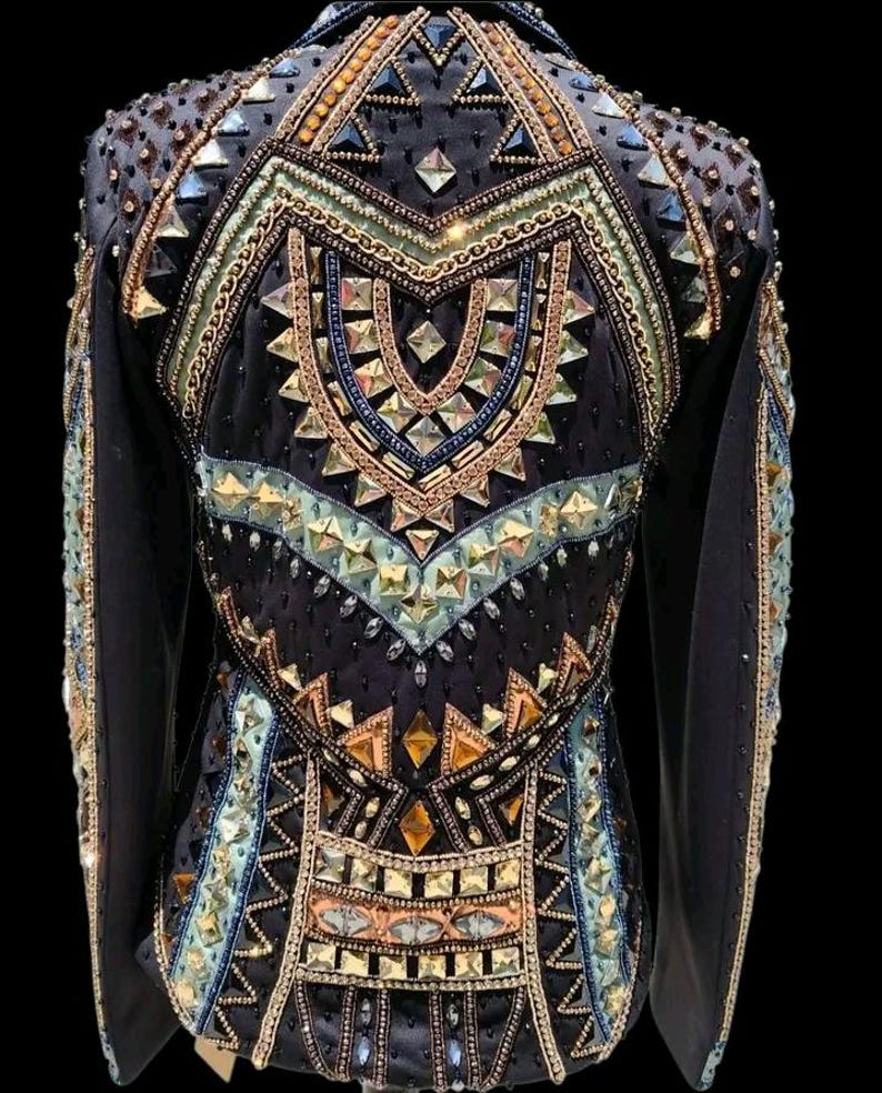 K&ouml;nnte beinhalten: Eine schwarze Langarmjacke mit einer komplexen Anordnung aus geometrischen Kristallen, Metallnieten und Perlen in Gold-, Bronze- und Hellblaut&ouml;nen, die ein symmetrisches Muster auf dem R&uuml;cken und den &Auml;rmeln bilden.