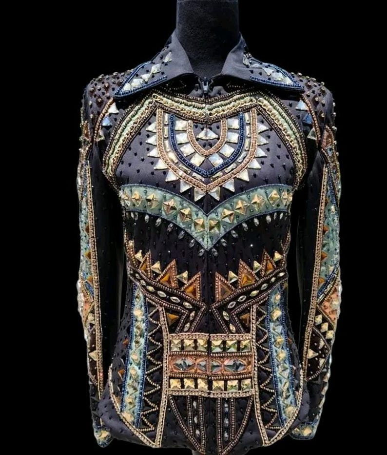 K&ouml;nnte beinhalten: Ein schwarzes Langarmshirt mit hohem Kragen und Frontrei&szlig;verschluss. Das Kleidungsst&uuml;ck ist reich verziert mit geometrischen Mustern aus Metallnieten, klaren Kristallen und bernsteinfarbenen Steinen, die in symmetrischen Reihen angeordnet sind.