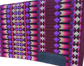 May include: A rectangular, woven saddle pad with a burgundy base. The pad features a repeating pattern of pink, purple, and cream-colored geometric shapes. A black leather patch is sewn on the bottom corner. The pad is designed for equestrian use.
