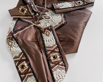 May include: A brown, embellished jacket and matching sleeve cuffs. The jacket features intricate beadwork in white, gold, and burgundy, with geometric patterns. The fabric has a subtle sheen, and the cuffs mirror the jacket's design. The overall style is ornate and detailed.